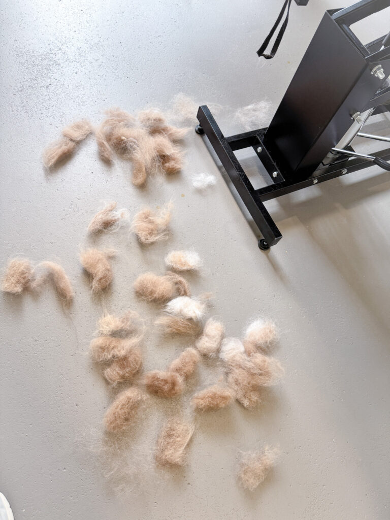 A close-up of piles of removed dog undercoat fur on a grey floor.