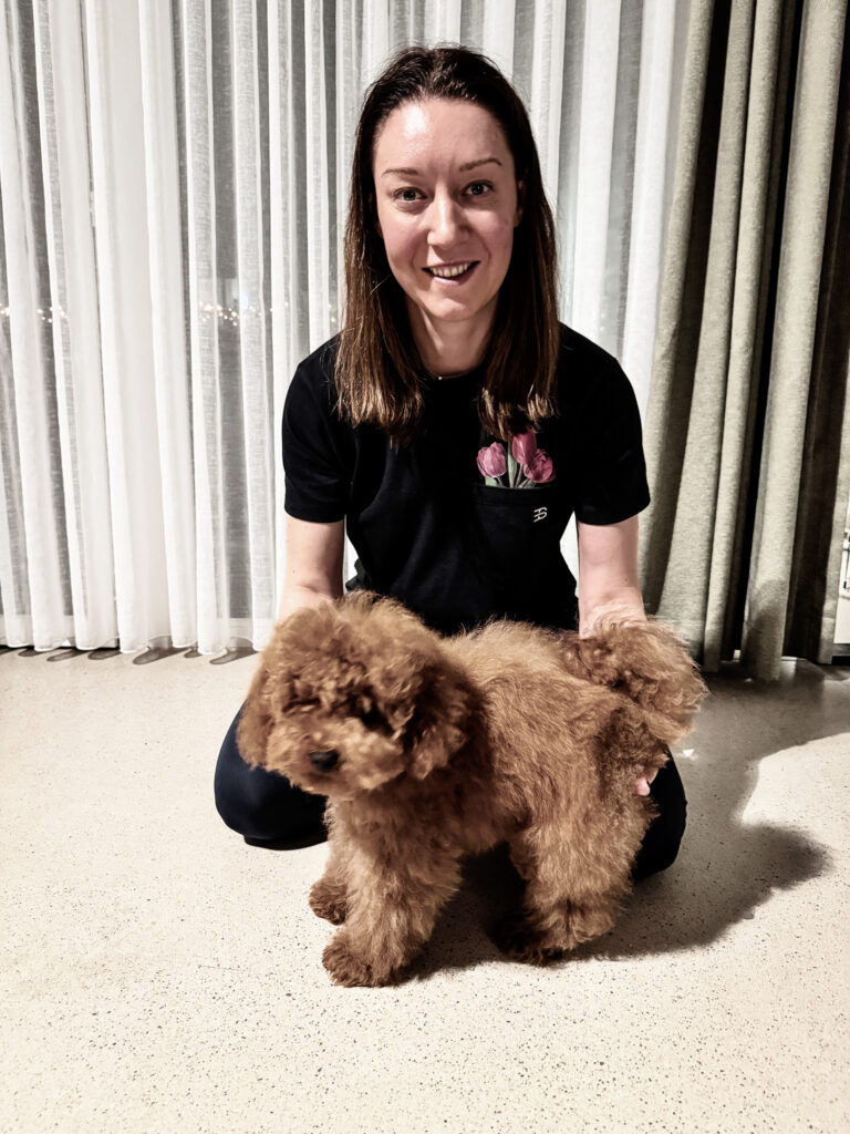 Woman kneeling indoors while gently supporting a fluffy brown puppy